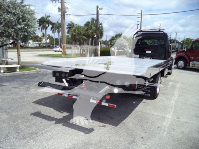Flatbed tow truck in a parking lot, Freightliner M2 106 rollback with rear loading bed and hydraulic ramps visible.