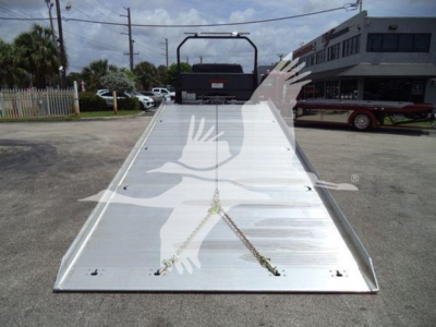 Aluminum rollback truck bed on a Freightliner M2 106 with chrome surface and safety chains, view from front with vehicle in background.