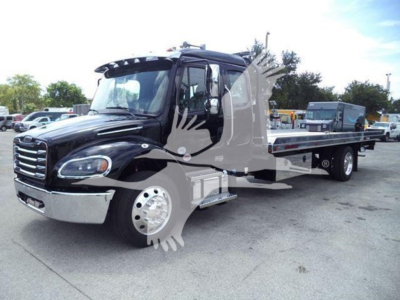 Truck cab and rollback bed showing Freightliner M2 106 with black exterior and chrome bumper, side steps, and long flatbed in a dealership lot.