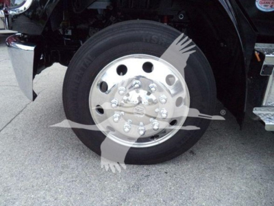 Truck wheel assembly showing large chrome hubcap and tire on Freightliner M2 106, with partial vehicle frame and fender visible.