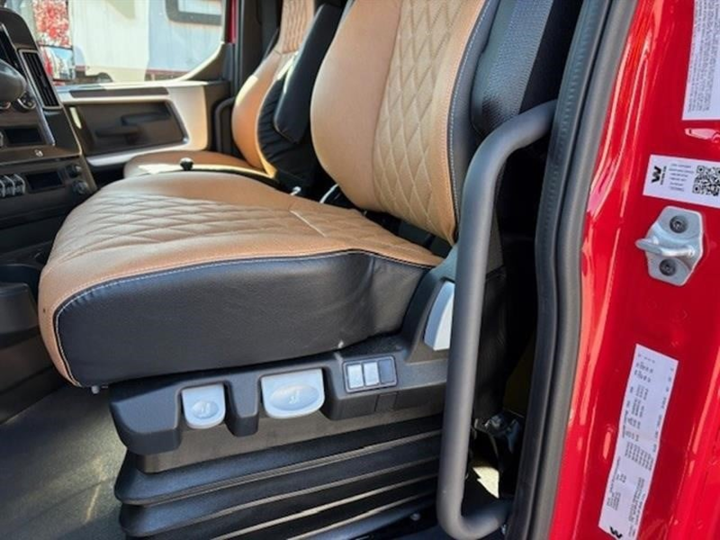 Interior driver seat area of a 2026 Western Star 49X dump truck showing tan leather seats with diamond quilting, seat controls, and door jamb area.