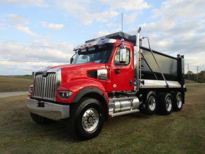 Red Western Star 49X dump truck with black dump bed, front chrome bumper, large grille, and multiple rear axles on grassy lot.