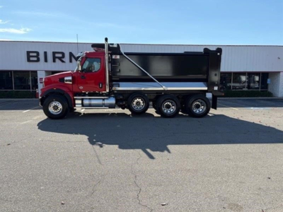 Red Western Star 49X dump truck in side profile showing dump bed and rear tandem axles parked in lot.
