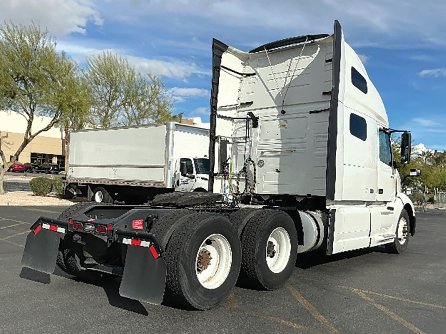 Volvo VNL 760 semi-truck tractor rear and sleeper cab, white paint, triple rear axles, high-roof sleeper, with fifth wheel and mud flaps.
