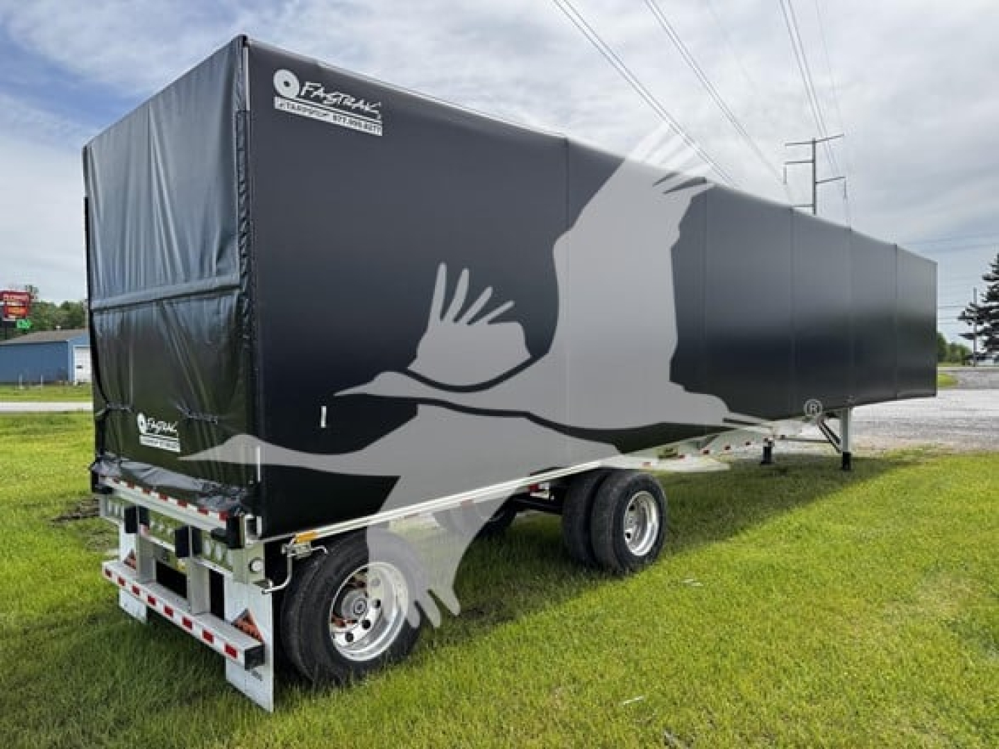 LK trailer side view showing curtain-side cargo trailer with black tarp and white graphic silhouette on dual-axle chassis.