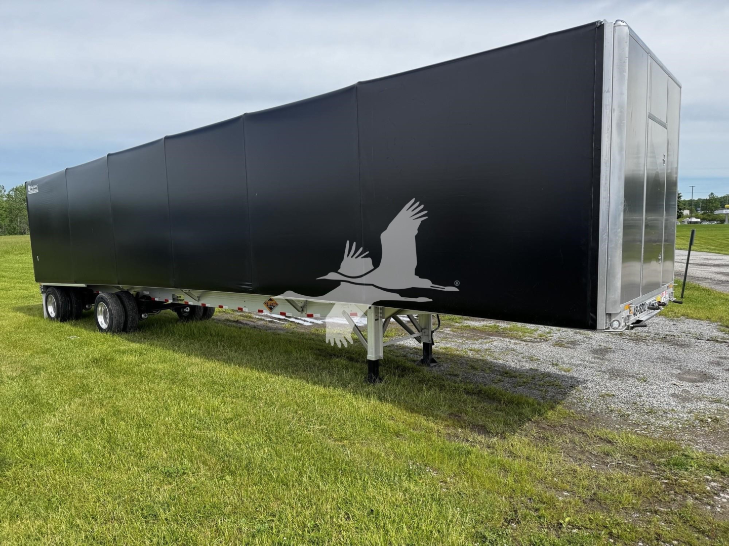Curtainside trailer in service view showing black side panels and a silver front corner; logo of a bird in flight on the side; trailer on dual-axle wheels, elevated landing gear visible.