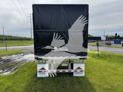 Curtainside trailer rear view showing black tarp and reflective rear with light bars.
