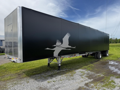 Curtainside trailer showing black sides with white bird silhouette, tandem axle, front landing gear, metal rear doors, and reflective trim.