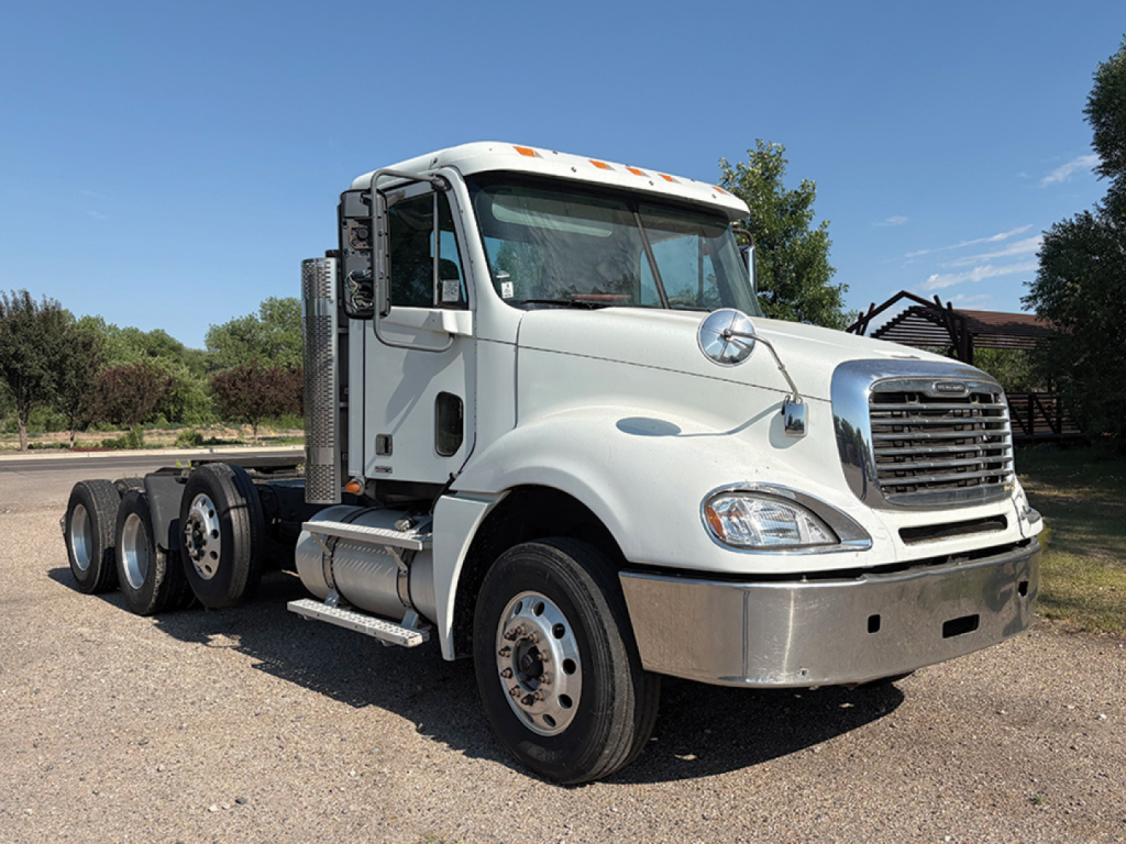White 2011 Freightliner CL120 Columbia daycab truck in a gravel lot, front three-quarter view, chrome grille, dual rear axles, fuel tanks, and running boards visible.