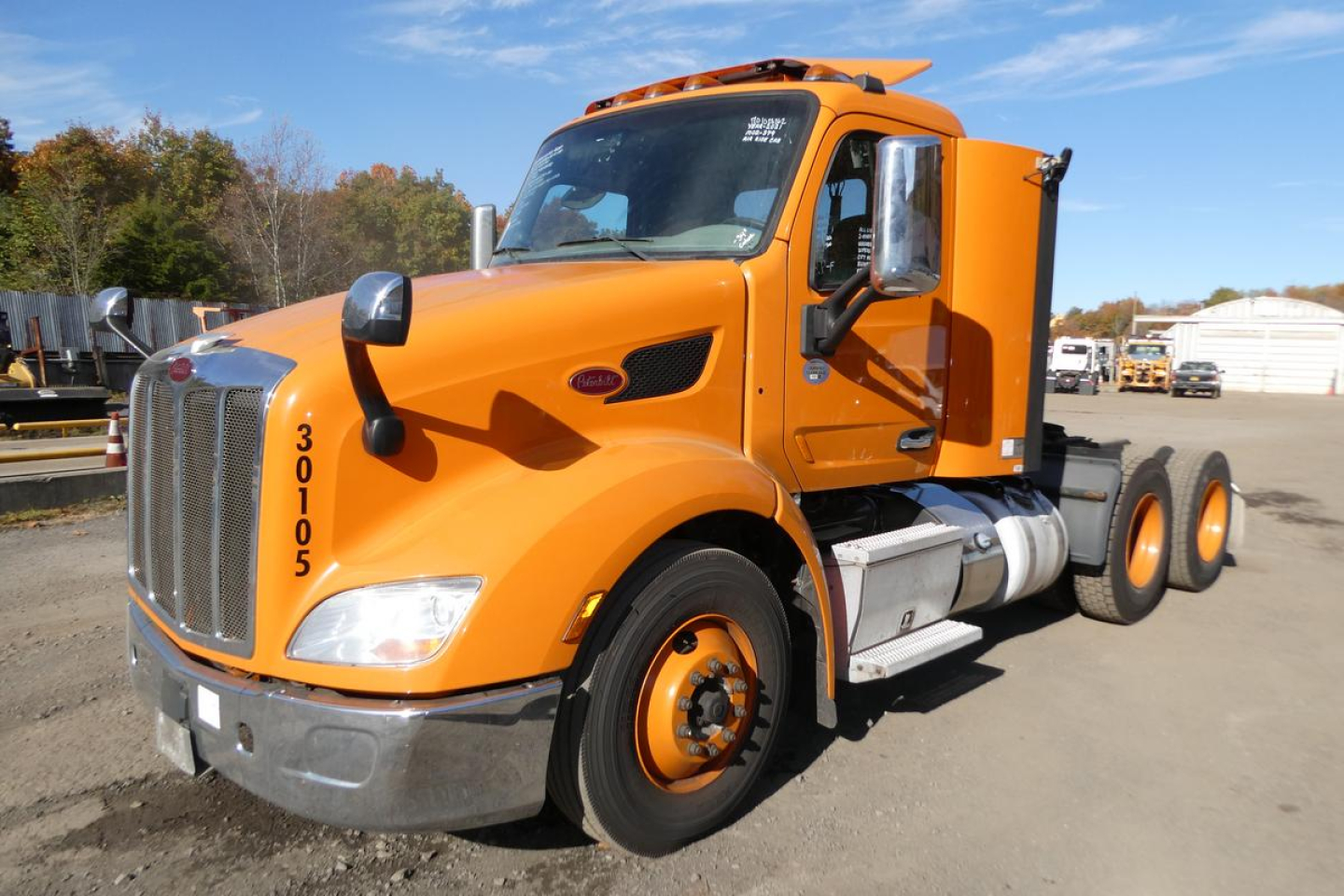 Peterbilt 579 conventional daycab truck in orange, front-left view, showing cab and chassis with dual rear axles and silver fuel tanks.
