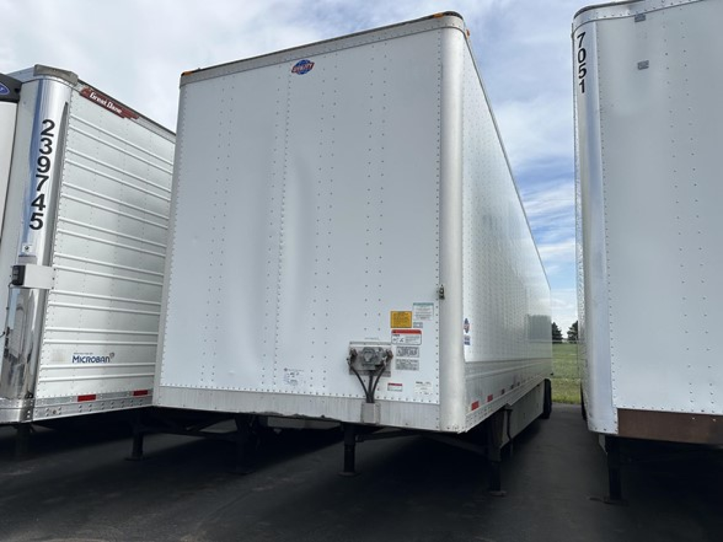 Utility 4000D-X trailer front view showing plain aluminum side with hinge and support legs, identification stickers, and hitch area.
