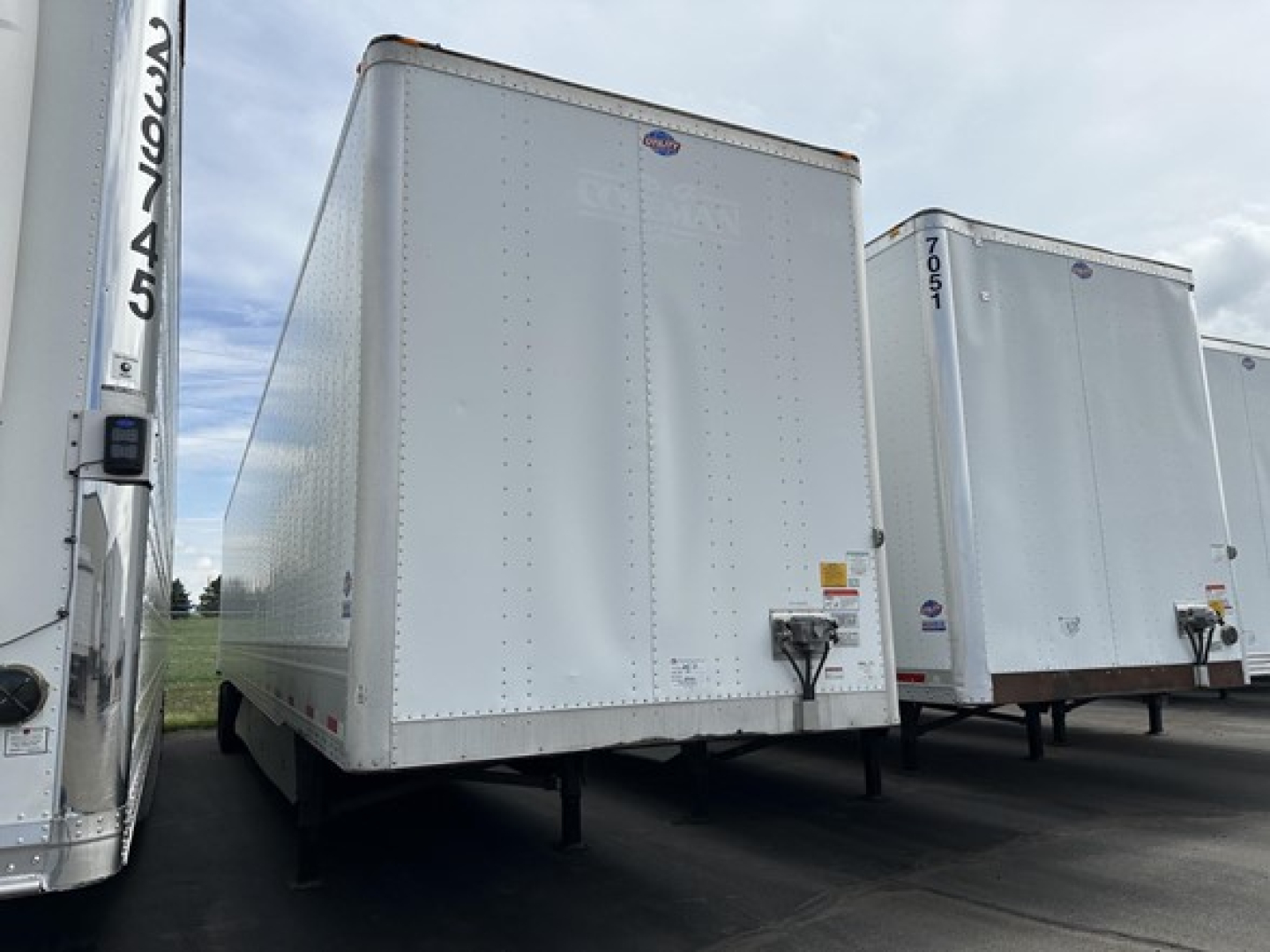 Trailer side view showing a white Utility 4000D-X box trailer with front door and hitch, other trailers in background.