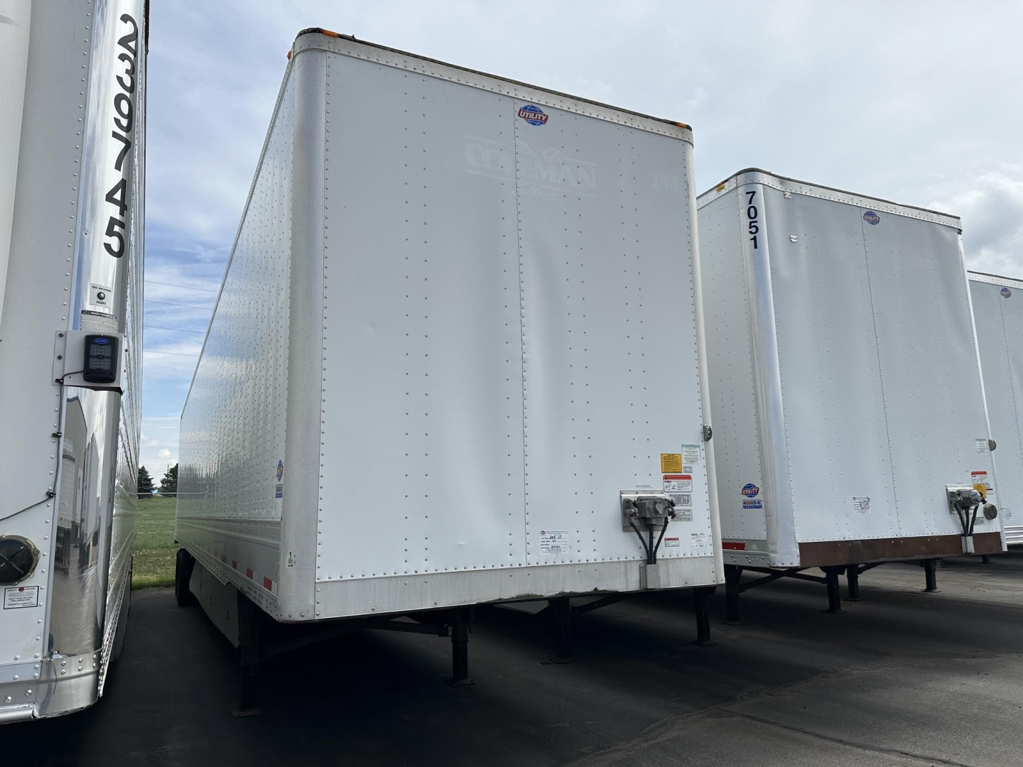 Flatbed utility trailer box with plain white exterior, front corner view showing DOT/brand stickers, hitch and support legs visible.