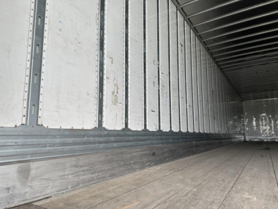 Trailer interior with metal side walls and wooden floor, empty cargo area showing ribbed wall panels and ceiling beams.