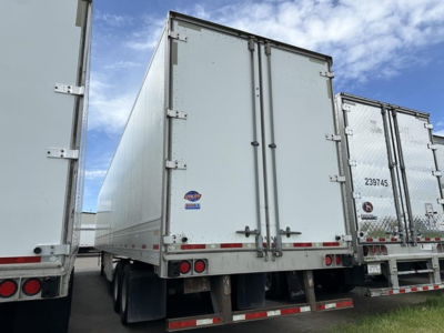 Utility 4000D-X trailer with closed rear doors, side hinges, and reflective tape; visible VIN/stock on a sticker; other trailers parked nearby.