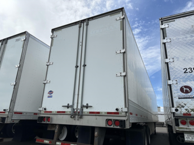 Rear view of Utility trailer with double doors, white/gray metal sides, red/white reflective tape. Visible text includes 'GRO' or 'GORT' on door, small blue sticker, warning lights, and rear bumper area.