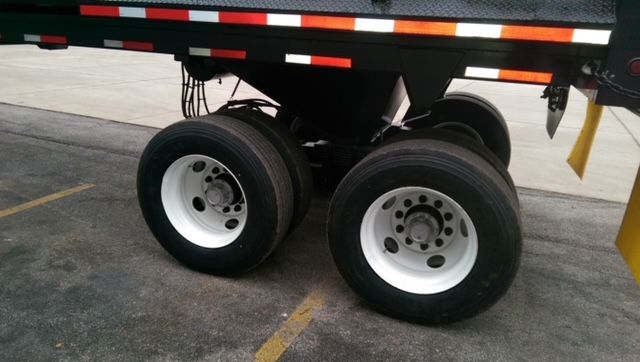 Dual rear wheels of a dump trailer with white rims and black tires; visible frame and reflective tape. No legible labels or text visible on components in this view.