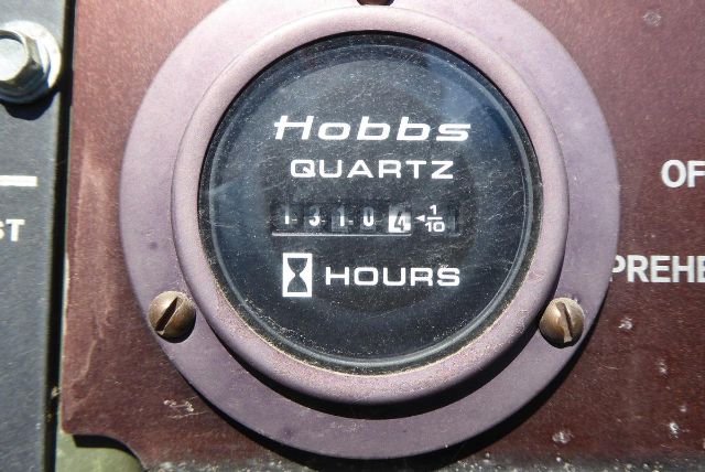 Hobbs QUARTZ hours meter showing 14910.1 hours (1/10) on brown panel with screws.
