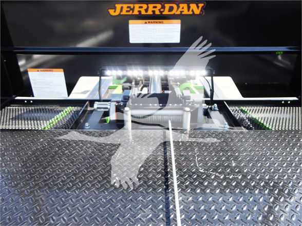 Vehicle platform with diamond plate surface and JERR-DAN branding on equipment, warning labels, and a mechanical linkage in the center.