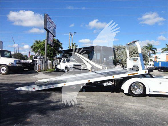 Tow truck flatbed with a long aluminum deck and white cab, International MV in dealership lot.