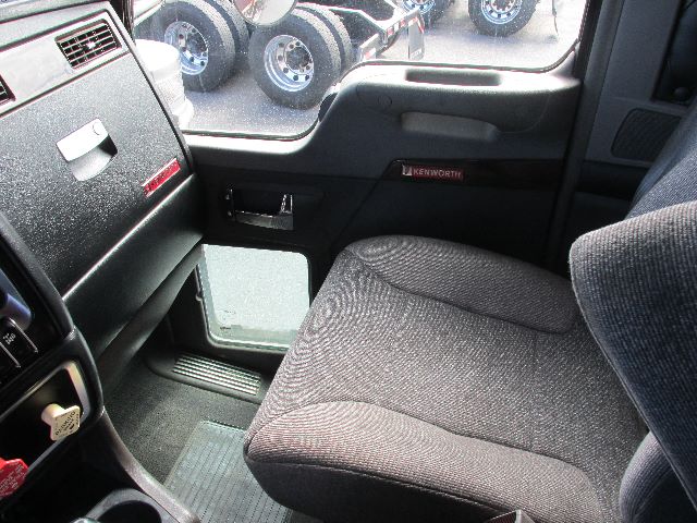 Interior cab of a Kenworth W900 truck showing steering wheel area, passenger seat, and door panel with Kenworth badge.