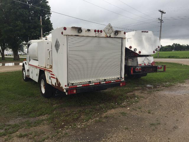 Freightliner FL-70 service truck rear view with large metal storage box, roll-up compartment door, and utility lights.