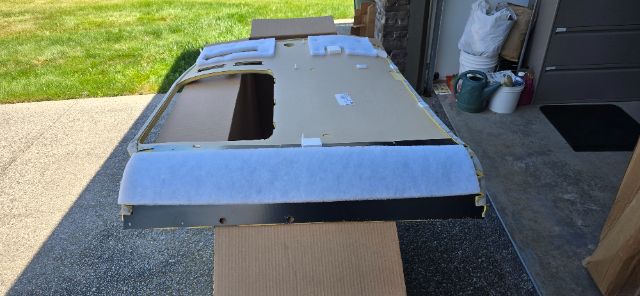 Truck sleeper roof panel with cutouts and mounting tabs, assembled on cardboard, outer surface light gray; visible in driveway.