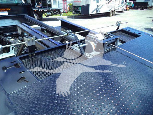 Truck bed with safety rails and hydraulic components visible, diamond plate surface, some equipment mounted on center area.