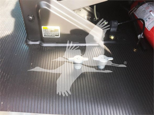 Two white tow hooks/anchors on a ribbed metal floor with a flame-like logo in the center and part of a equipment unit with warning label visible.