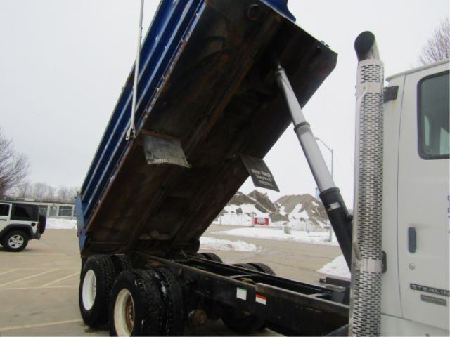 Dump truck with raised blue dump bed showing hydraulic cylinder and side exhaust, wheels and chassis visible.