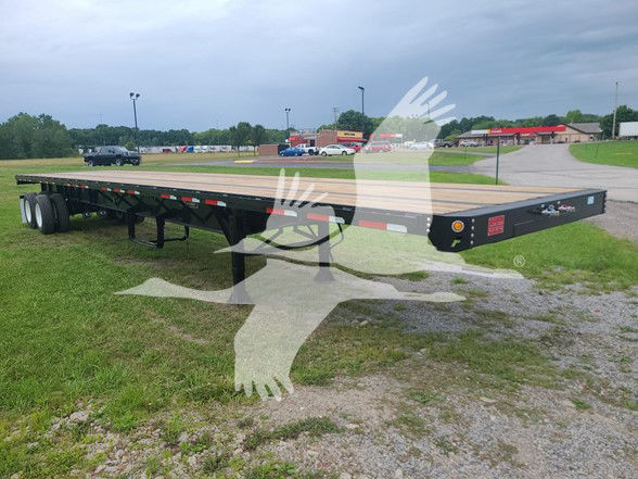 Fruehauf steel flatbed trailer with long black chassis and wooden deck, dual rear axles with white wheels, located in a lot with other vehicles.