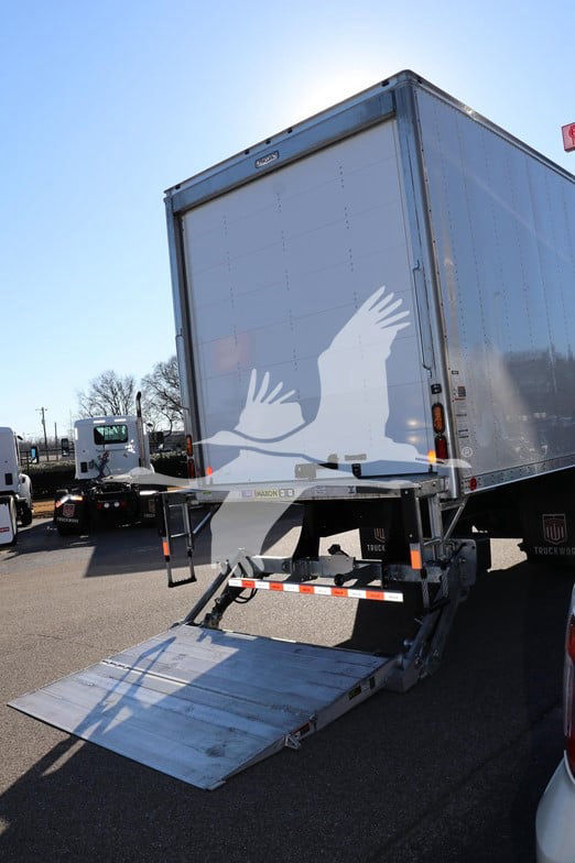 Isuzu box truck with a hydraulic liftgate deployed at the rear, loading ramp extended, metal sides and back doors visible.
