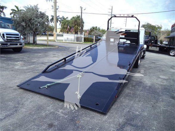 Tow truck flatbed with black metal ramp and winches, rear loading area, and safety rails visible; Mack MD6 listing details in the background.