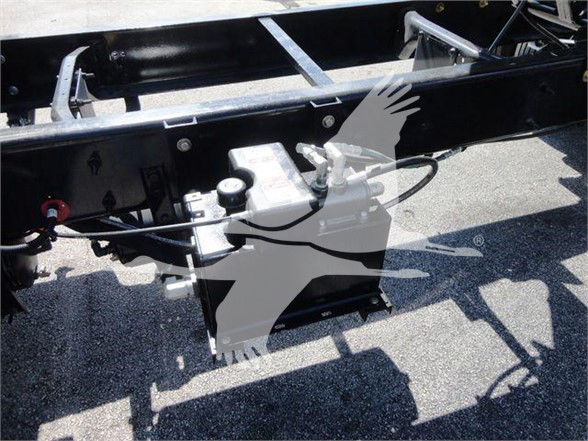 Vehicle chassis with hydraulic reservoir and control valve assembly mounted under a truck frame, showing hoses and mounting hardware.