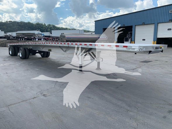 Flatbed trailer in outdoor lot showing long aluminum deck with dual rear axles and reflective tape along sides.