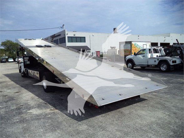 Truck bed tilted in loading position showing tow truck with flatbed and ramp on a dealership lot.