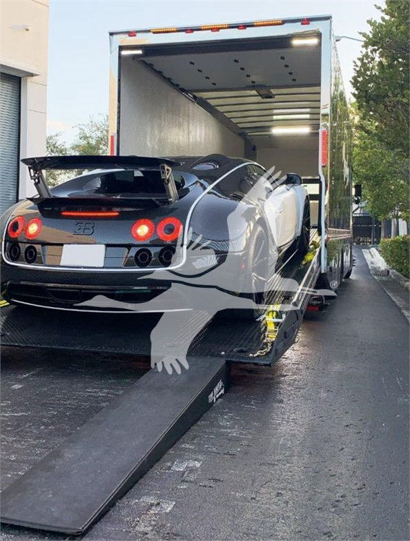 2022 Peterbilt 337 being loaded into an enclosed car trailer; rear of grey sports car visible, ramp extended.