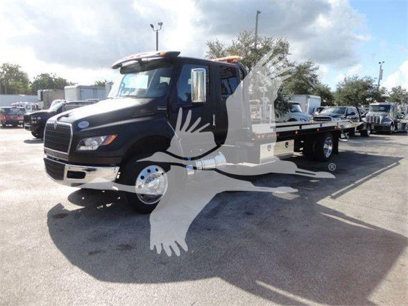Black International MV tow truck with flatbed, front grille and cab visible. Vehicle appears in a dealership lot with other trucks in background. No legible text on visible surfaces.