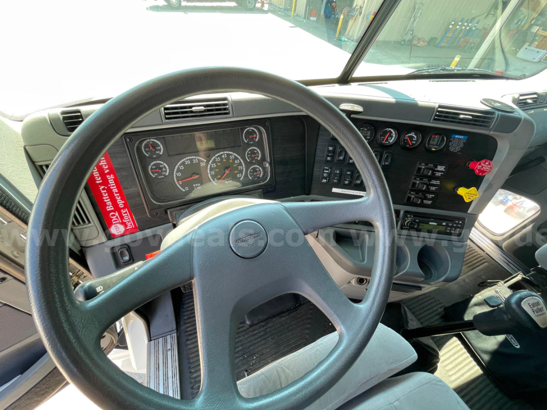 Freightliner Columbia 120 cab interior showing steering wheel, dashboard gauges, and gear shifter.