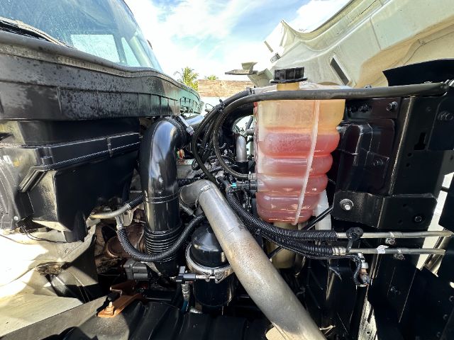 Truck engine bay with coolant reservoir and various hoses; pinkish coolant in translucent reservoir, black hoses, metal pipes, and engine components visible.