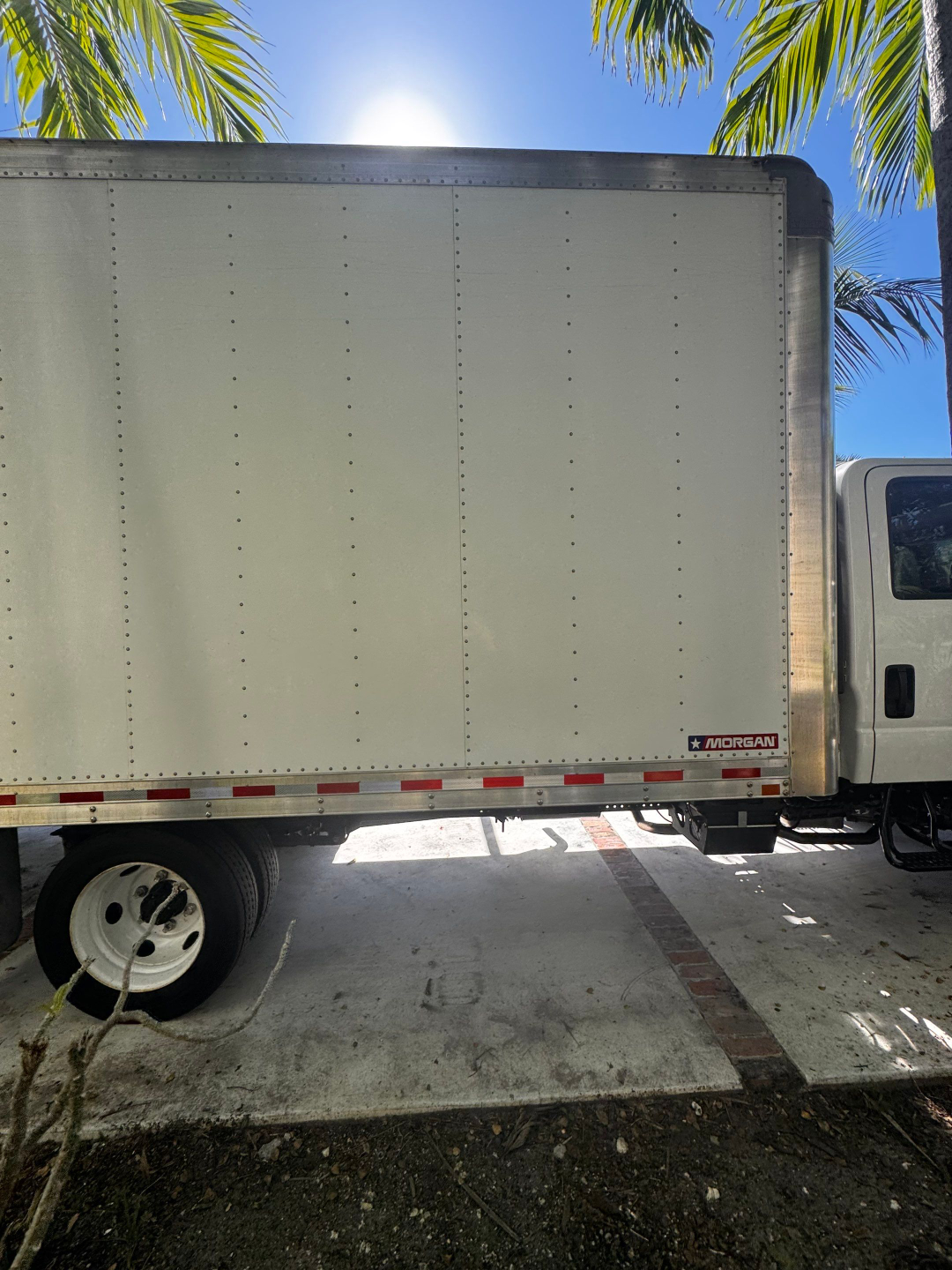 Box truck side panel with riveted aluminum walls and Morgan logo near bottom edge; single rear wheel visible.