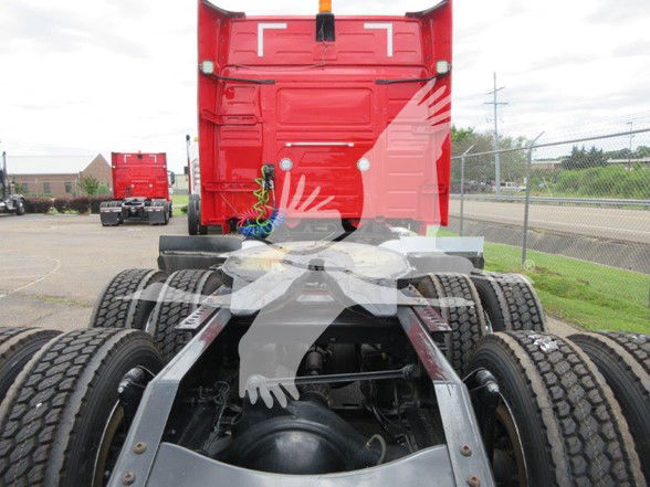 Truck chassis view showing Volvo VNL64T740 rear with dual rear axles and fifth wheel plate, red sleeper cab visible in background, visible drivetrain components.