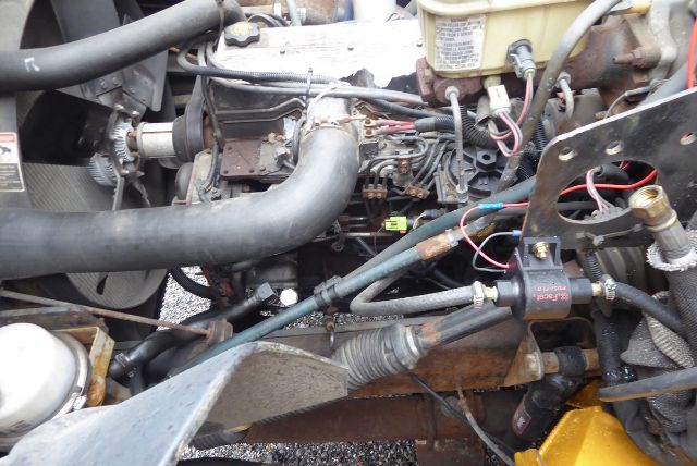 Engine bay of Freightliner FS65 with hoses, belts, and wiring harness visible; turbo/manifold area and radiator hoses in view.