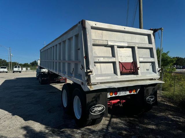 Dump trailer showing rear view with galvanized dump bed, dual rear wheels, CRMP mud flaps, and hydraulic mechanism at the back.