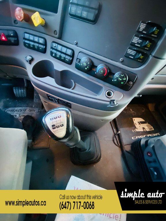 Interior of a Freightliner Cascadia truck with manual gear shift, dashboard controls, cup holders, and floor mats.