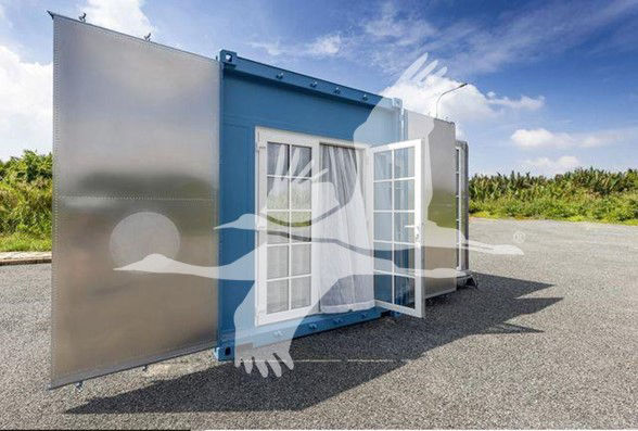 Trailer with blue central module and two large mirrored panels on the sides; a white-framed window/door is open in the blue module; outdoor lot with clear sky.