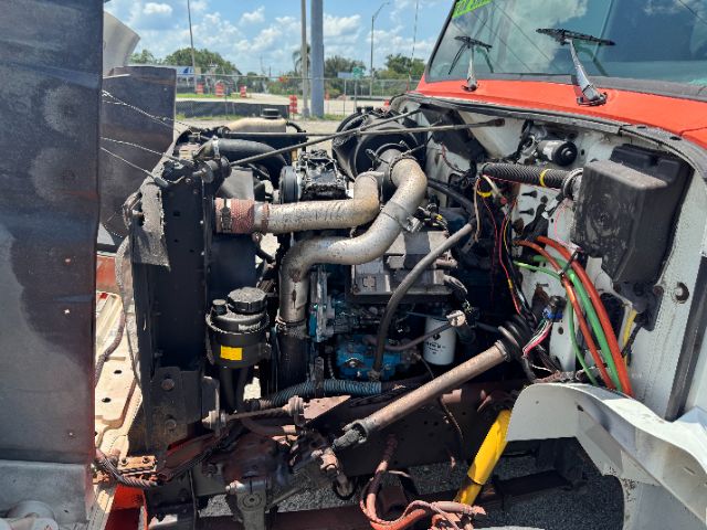 Truck engine bay of a 1999 International 4700 DT 466E showing engine components, hoses, and wiring in view from the front-left side.