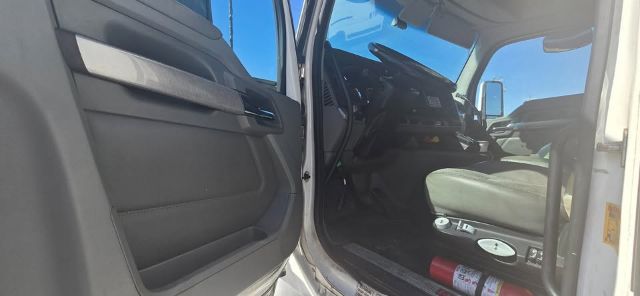 Kenworth T680 interior cab view from open driver door showing steering wheel and dashboard, light gray seats, and door panel.