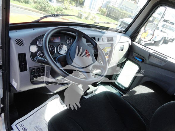 Fractions of dashboard and steering wheel of a 2022 Peterbilt 337 interior visible with gauges and steering wheel, side window showing exterior lot.