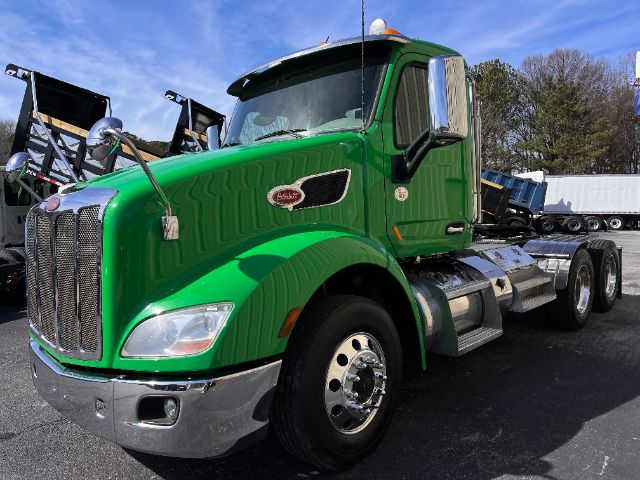 Green 2018 Peterbilt 579 conventional daycab truck, side view showing chrome front grille, large fuel tanks, and dual rear axles.